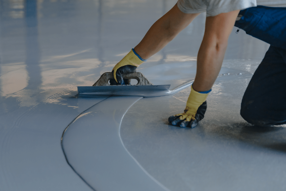 The worker applies gray epoxy resin to the concrete floor